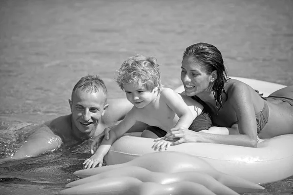 Vader en moeder in de buurt van matras zwemmen met zoon. Familie besteden tijd samen en plezier. Schattig kind jongen zit op luchtbed ananas gevormd in de oceaan met ouders. Familie vakantie concept — Stockfoto