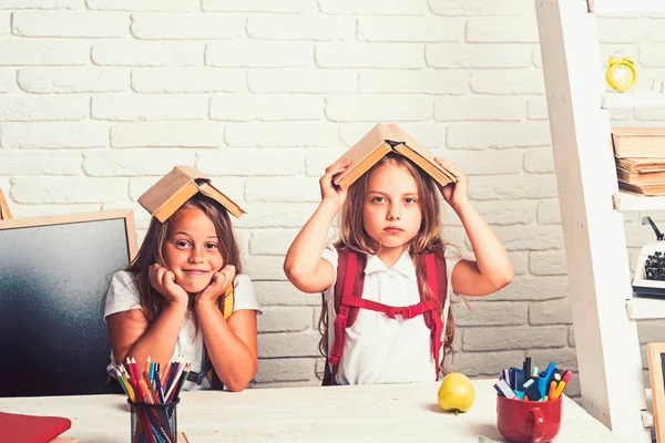 Hora da escola das raparigas. Amizade de irmãs pequenas em sala de aula no dia do conhecimento. De volta à escola e à escola em casa. crianças da escola triste na lição em setembro 1. Meninas com livros na cabeça — Fotografia de Stock