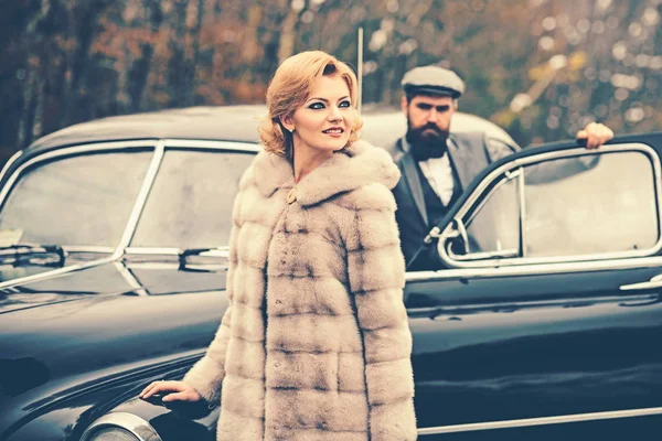 Travel and business trip or hitch hiking. Bearded man and sexy woman in fur coat. Retro collection car and auto repair by mechanic driver. Couple in love on romantic date. Escort of girl by security.