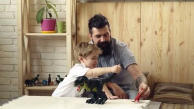 Sevimli küçük çocuk sakallı babasıyla plastik dinozorlarla oynuyor. Oğul ve baba, büyük Tyrannosurus ve küçük dinozor arasındaki savaş savaşında oynuyorlar. Çocuk için ilginç bir hediye..