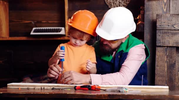 Junge, Kind mit Schutzhelm, das mit Papa Schraubenzieher lernt. Teamwork im Werkstattkonzept. Vater, Elternteil mit Bart bringt kleinem Sohn Werkzeugschraubendreher bei. — Stockvideo