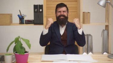 Genç adam ofiste başarı kutlamaları yapıyor. Başarı ve başarı kavramı. Ofiste oturan mutlu beyaz sakallı adam kazanan jestler yapıyor. Her gün kazanan. İş başarısı sonuç kavramını kazandı.