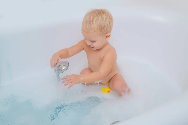 Härligt barn leker med skum. Kid i badkaret med badkar. Rolig söt bebis simmar i skum i badet. — Stockfoto