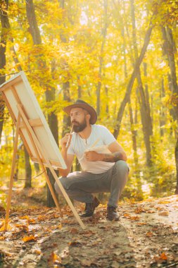 Ressam ormanı. Sanat konsepti. Doğada resim yapmak. Yeni bir filme başla. Tablo ve tuvalli bir ressam. Sakallı adam ressam, sonbahar doğası için ilham arıyor. Rahatla ve hobi olarak. Hayattan çizim