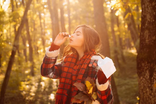 Rapariga espirrando com limpador de nariz entre árvores amarelas no parque. A mulher faz uma cura para a constipação comum. A mostrar a mulher doente a espirrar no parque de Outono. Jovem com limpador de nariz perto da árvore de outono — Fotografia de Stock