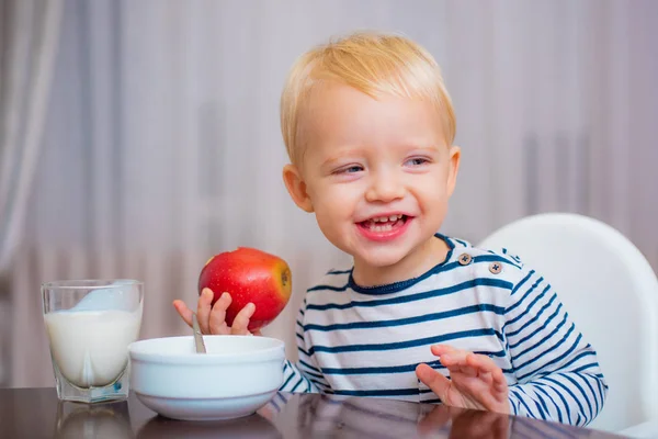 Een leuke jongen zit aan tafel met bord en eten. Gezond eten. Een leuke baby die ontbijt eet. Babyvoeding. Eet gezond. Peuter neemt een snack. Gezonde voeding. Vitamine concept. Kind eet appel — Stockfoto