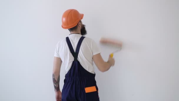 Visão traseira do pintor homem pintando a parede, com rolo de pintura isolado em grande espaço vazio. Conceito de obras de reparação. Espaço para cópia. Parede de pintura de rolo. homem com tatuagens pintado uma parede com um rolo . — Vídeo de Stock