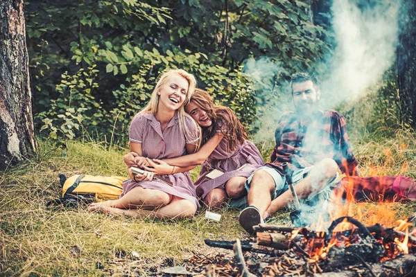 Witze am Lagerfeuer erzählen. lachende Freunde, die im Wald zelten. Rauch vom Lagerfeuer bedeckt die Menschen — Stockfoto