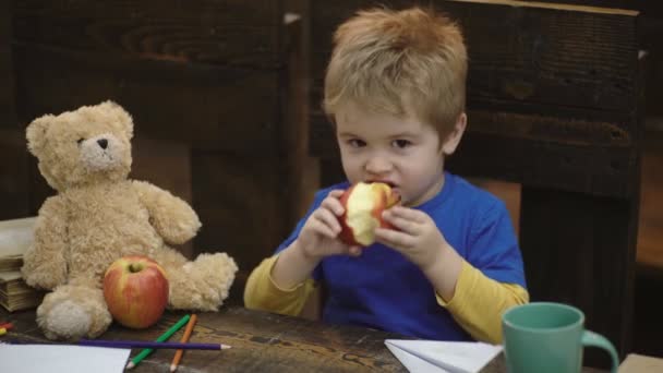 Schulpause. Hungriges Kind isst Apfel im Klassenzimmer. kleiner Junge am Schreibtisch vor der Tafel, der Apfel isst. Schüler bei einem Apfel in der Mittagspause. gesunde Kost für Kinder. Zurück zur Schule. — Stockvideo