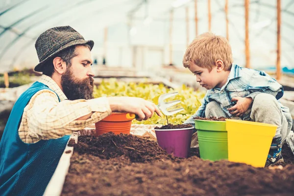 側面ビュー父手フォークで花を植えるための子供を助けること。息子のガーデニングを教えるひげを生やした男。家庭教育概念 — ストック写真