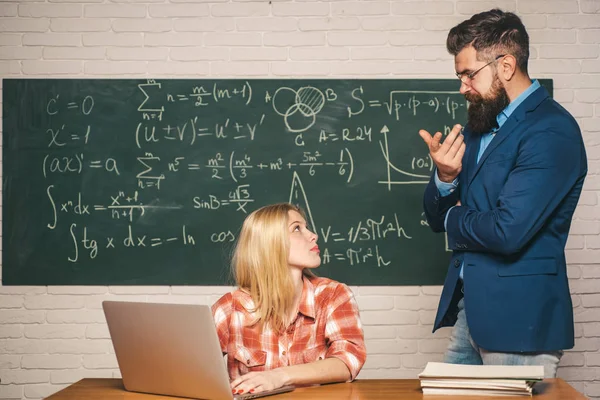 Team collaboration concept. Young teacher near chalkboard in school classroom. Education and learning people concept - female student and Teacher. Teacher job - profession and learning concept.