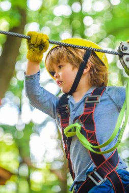 Ağaç evde ya da halat parkında güvenlik ekipmanlarına tırmanan sevimli bir çocuk ipe tırmanıyor. Mutlu küçük çocuk halatla oyun sahasına tırmanıyor..
