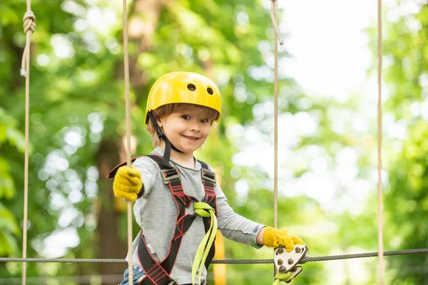 Happy child boy calling while climbing high tree and ropes. Portrait of a beautiful kid on a rope park among trees. Small boy enjoy childhood years.