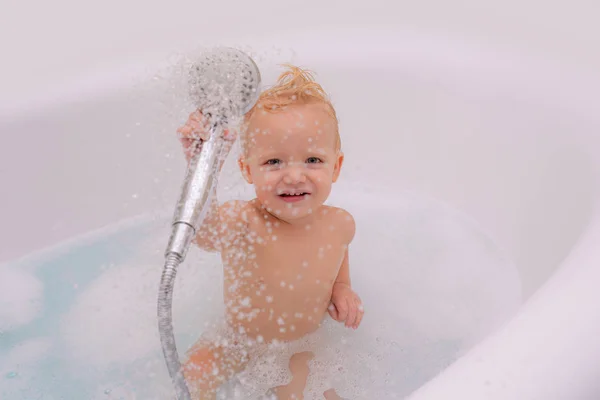 Αστείο μωρό παίζει με το νερό και αφρό σε ένα μεγάλο νεροχύτη κουζίνα. Μικρό παιδί σε μια μπανιέρα. — Φωτογραφία Αρχείου