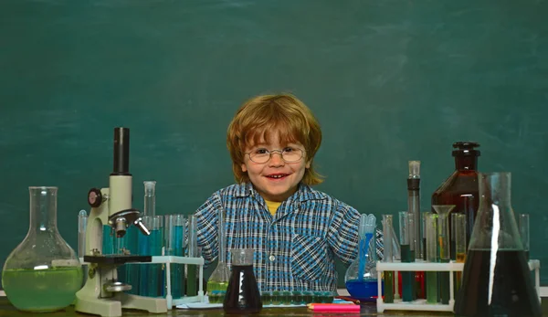 Glad leende liten pojke ha kul mot Blue Wall. De genomförde ett nytt experiment i kemi. Förskolebarn. Barn i klassrummet med svart tavla på bakgrunden. Utbildning — Stockfoto