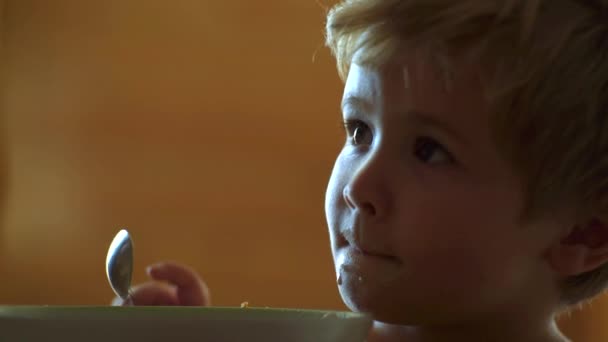 Bebé comiendo. Un niño desayunando en la cocina. La cuchara de niño feliz se come sola. Bebé comiendo comida en la cocina. Alegre bebé niño come comida sí mismo con cuchara . — Vídeos de Stock