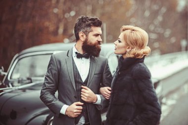 Couple in love on romantic date. Bearded man and sexy woman in fur coat. Retro collection car and auto repair by mechanic driver. Travel and business trip or hitch hiking. Escort of girl by security. clipart