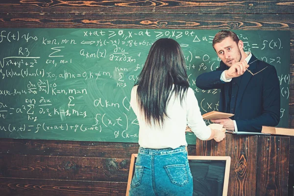 Estudante e professor discutindo em sala de aula. Menina vista traseira em jeans azul e jumper branco em pé na frente do rostrum durante a palestra — Fotografia de Stock