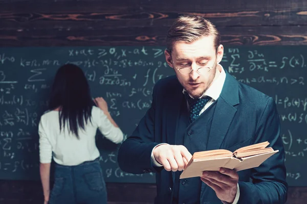 Konzentrierter Professor liest der Klasse Artikel vor, während junge Studentin an Bord schreibt — Stockfoto