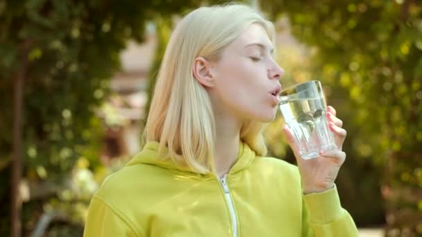 Όμορφο κορίτσι που πίνει νερό από γυαλί στο πράσινο πάρκο. Καθαρό νερό υγείας κονέ. — Αρχείο Βίντεο