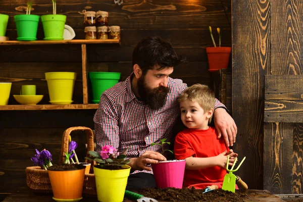 Flower care watering. Soil fertilizers. Father and son. happy gardeners with spring flowers. bearded man and little boy love nature. Family day. Greenhouse. Working with plants is great pleasure