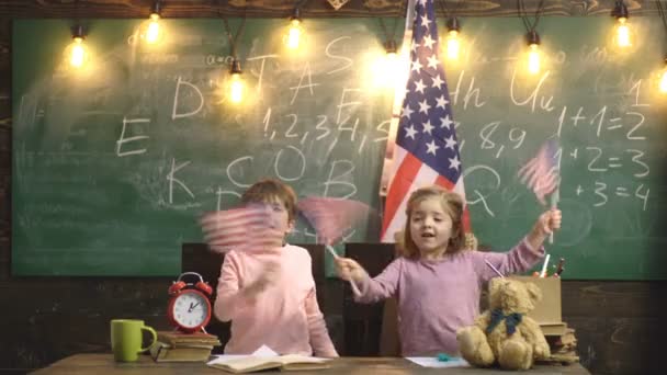 Ragazza e ragazzo sventolano bandiere americane a scuola. Il concetto del Giorno dell'Indipendenza. Felice adorabile bambina bionda caucasica e ragazzo sorridente ridere e sventolare bandiera americana che celebra il 4 luglio . — Video Stock