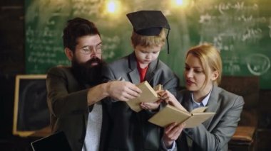 Okula geri dön. Dahi oğlu anne ve baba öğrenciler için kitap okudu. Dizüstü bilgisayar ile masada birlikte aile çalışma. Küçük çocuk kadın ve erkekle okul oynuyor. Mezuniyet şapkalı çocuk. Öğrenme kavramı