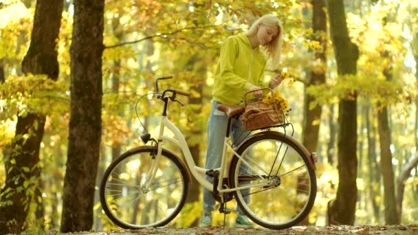Τα κορίτσια χέρια κρατούν παλιό τιμόνι ποδηλάτου με λουλούδια καλάθι. Όμορφη νεαρή γυναίκα με ποδήλατο στο πάρκο. Ανέμελη γυναίκα. Φθινόπωρο και φύλλα πέφτουν όνειρα. Καλημέρα και ωραία μέρα. Φθινοπωρινή ομορφιά. — Αρχείο Βίντεο