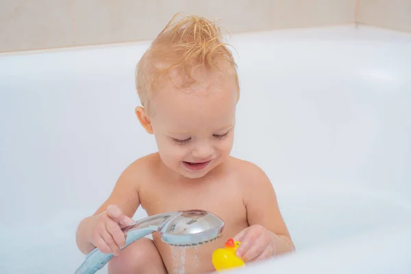 Красивый маленький мальчик принимает ванну с пеной. Игрушечная утка. Портрет улыбающегося ребенка. Детская стирка и купание . — стоковое фото