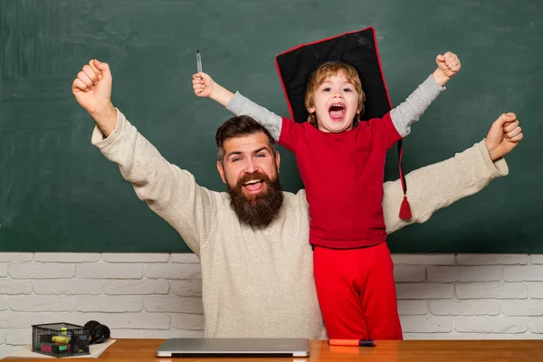 Hooray. Daddy and son raising clenched fists in hooray gesture. Father teaching her son in classroom at school. Yeah good work. Happy father and son over chalkboard. Daddy and son together.