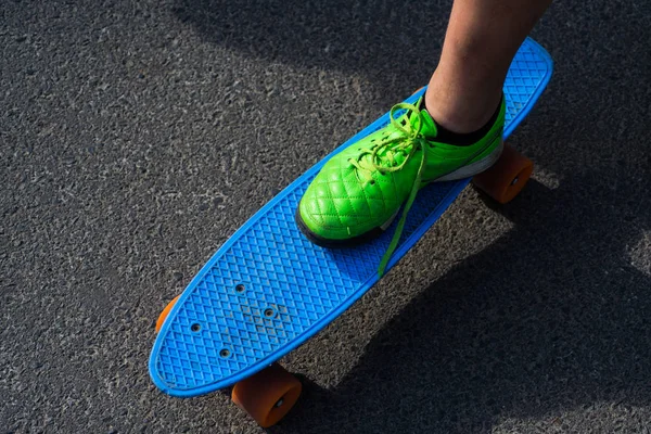 The only four wheels he can afford is a penny board. Male sneaker on blue penny board. Skateboarding or skating on skate board. Enjoy travelling on his plastic board — Stock Photo, Image