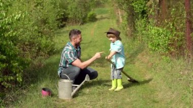 Baba ve oğlu, filizi tarlada suladılar. Tasasız çocukluk. Bahar tarlasında ekilen sakız botlu çocuk- çiftlikte baba oğul ve sebze. Genç çiftçi - baba oğul çiftçi