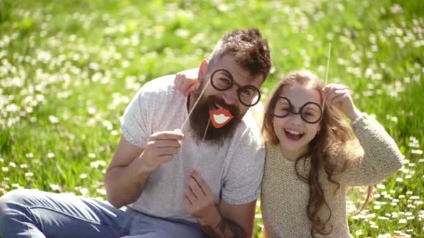 子と父 eyeglases でポーズ写真の草原でブース属性。スマートと巧妙な概念。お父さんと娘は草地、緑の背景に芝生の上に座っています。家族過ごすレジャー アウトドア. — ストック動画