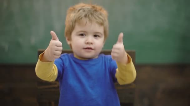 少年は緑の教育委員会の背景に対して親指を上げる。選択的な焦点。学校に戻れ学習コンセプト。手のジェスチャーを学ぶ。親指で彼の喜びを示す幸せな若い就学前の子供. — ストック動画