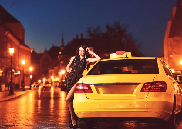 Девушка с гламурным макияжем. девушка в черном платье стоять у желтого автомобиля такси . — стоковое фото