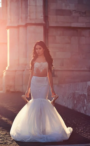 Vacker anbud ung kvinna sexig brunett brud i en lyx vit bröllop klänning håll skor på slott sommaren lyckan väntar brudgummen innan vigseln — Stockfoto
