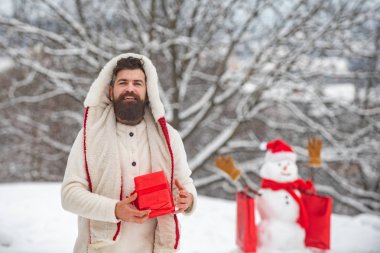 Mutlu mutlu baba ile güneşli kış gününde mutlu gülümseyen kar adam. Sevimli küçük kardan adam ve alışveriş çantası ile sakallı adam. Hipster Noel Baba. Teslimat hediyeleri.
