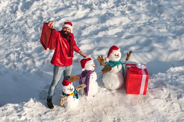 スタイリッシュな帽子と雪原のスカーフで面白い雪だるまと興奮した男。ギフト付きの幸せな冬の雪だるまの家族。母雪女、父雪男と子供は陽気なクリスマスと幸せな新年を願っています. — ストック写真