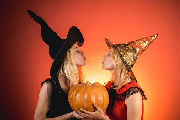 カボチャとオレンジ色の背景の上にパーティーにハロウィーンの衣装を着た2人の感情的な若い女性。魔女のカーニバルセクシーな衣装で2人の美しい女性。分離されたイメージ。ハロウィーンコピースペース. — ストック写真