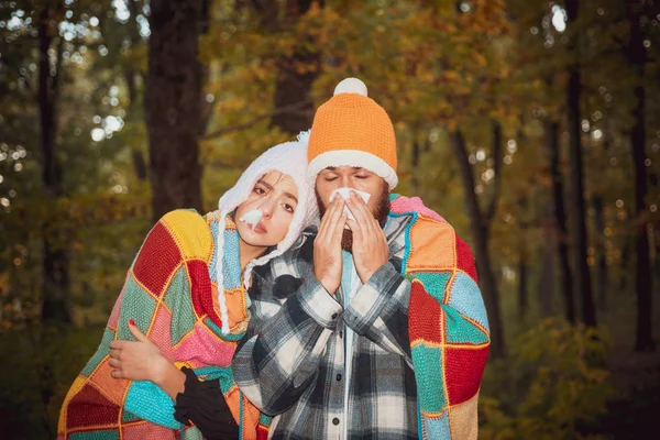 People sneezing in handkerchief autumn outdoor. People got flu, having runny nose. A young couple during disease treatment at autumn park background. Flu season, vaccination.