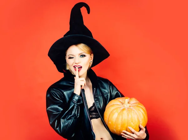 Legrační tvář a překvapena žena. ekret Halloween. Emotivní mladé ženy v halloweenových kostýmech na Rudém pozadí s dýní. — Stock fotografie