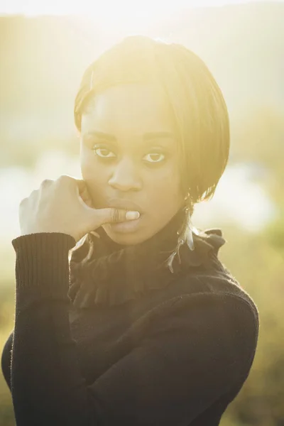 Afrikai kinézetű nő napfény, fény háttér, disszidált. A nyugodt arcú lány megérinti az érzéki ajkakat. Álmodozó és csábító lány megcsókolja a hüvelykujját. Afrikai csábítási koncepció — Stock Fotó