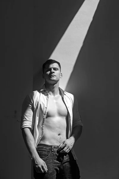 L'uomo in camicia aperta mostra busto sexy. Modello uomo con sguardo serio sulla parete soleggiata — Foto Stock