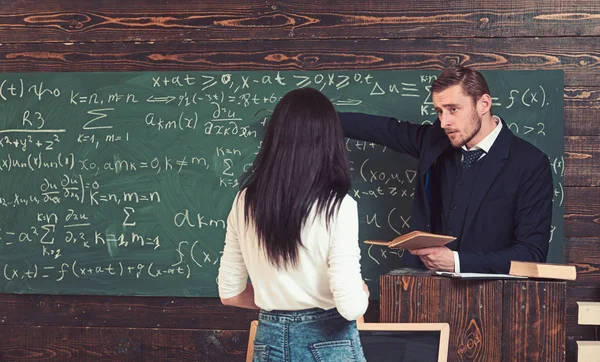 Matematiklärare pekar på gröna styrelse. Professor ger förklaringar till brunett kvinnlig student. Vända tillbaka flicka i vit jumper står framför talarstol — Stockfoto