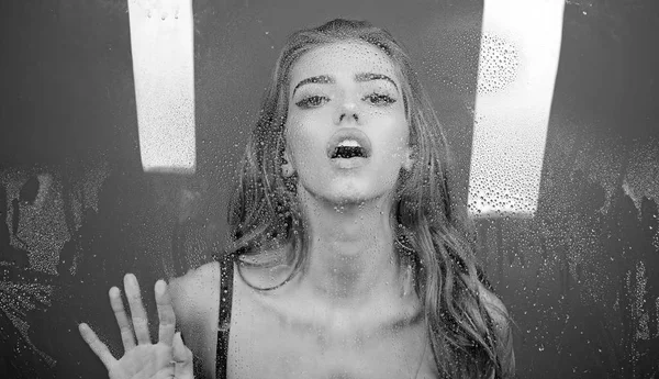 Sexy woman behind plastic sheet with water drops. Shower and hygiene spa treatment. Window with water drops before girl with makeup. Rain drops on window glass with face of girl. Fashion and beauty