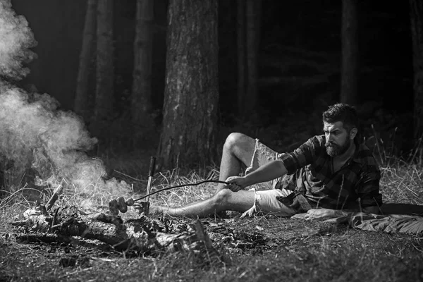 Одинокий турист бродит по лесу. Хипстер готовит сосиски над огнем. Босоногий лежал на траве. Кемпинг — стоковое фото