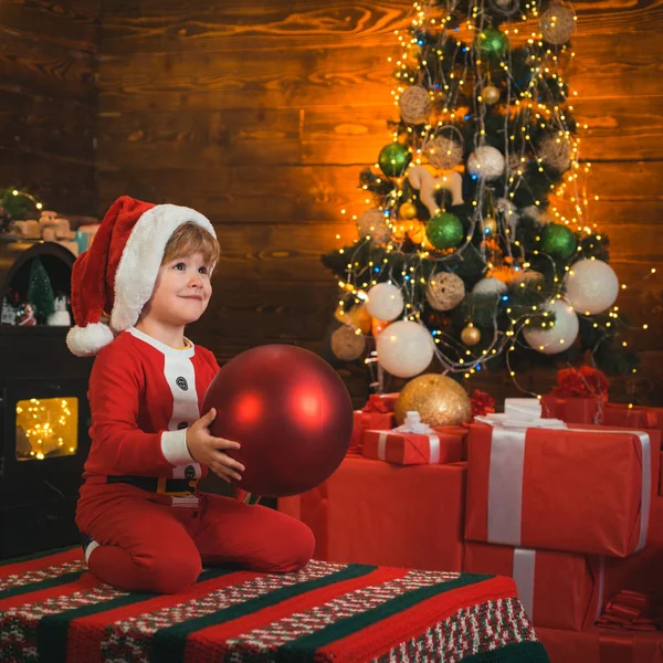 好きなおもちゃ赤ちゃんはクリスマスをお楽しみください。家族の休日。子供の頃の思い出サンタ少年の小さな子供はクリスマスを祝います。男の子はクリスマスツリーの近くで遊びます。新年のカウントダウン。陽気で明るいクリスマス — ストック写真
