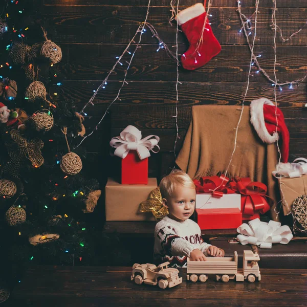 Crianças de Natal. Um miúdo engraçado a segurar um presente de Natal. Abrindo presentes no Natal e Ano Novo. Cartão de Natal. Retrato miúdo com presente no fundo de madeira . — Fotografia de Stock