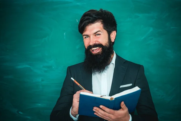 Profesor barbudo en la clase de la escuela en los escritorios en el aula. Educación. Joven profesor cerca de pizarra en el aula de la escuela. Profesor amable en el aula cerca del escritorio de pizarra. —  Fotos de Stock