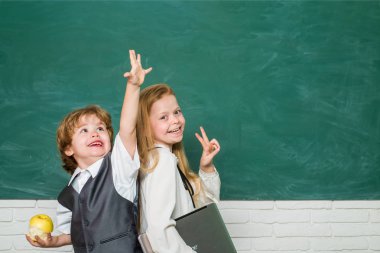 Çocuklar okula hazırlanıyor. Sınıfta bir çift küçük kız ve oğlan var. Öğrencilerin sınıftaki masalarda ders çalışmasına yardım eden liseli kız. Mutlu okul çocukları. Elma ve kitaplar - okul kavramı.
